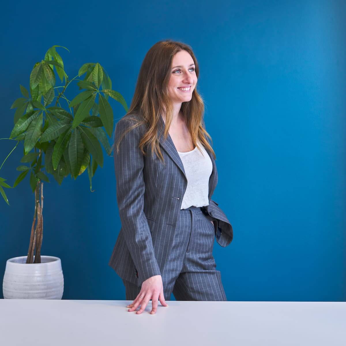 Une femme en costume d’affaires debout devant un mur bleu.